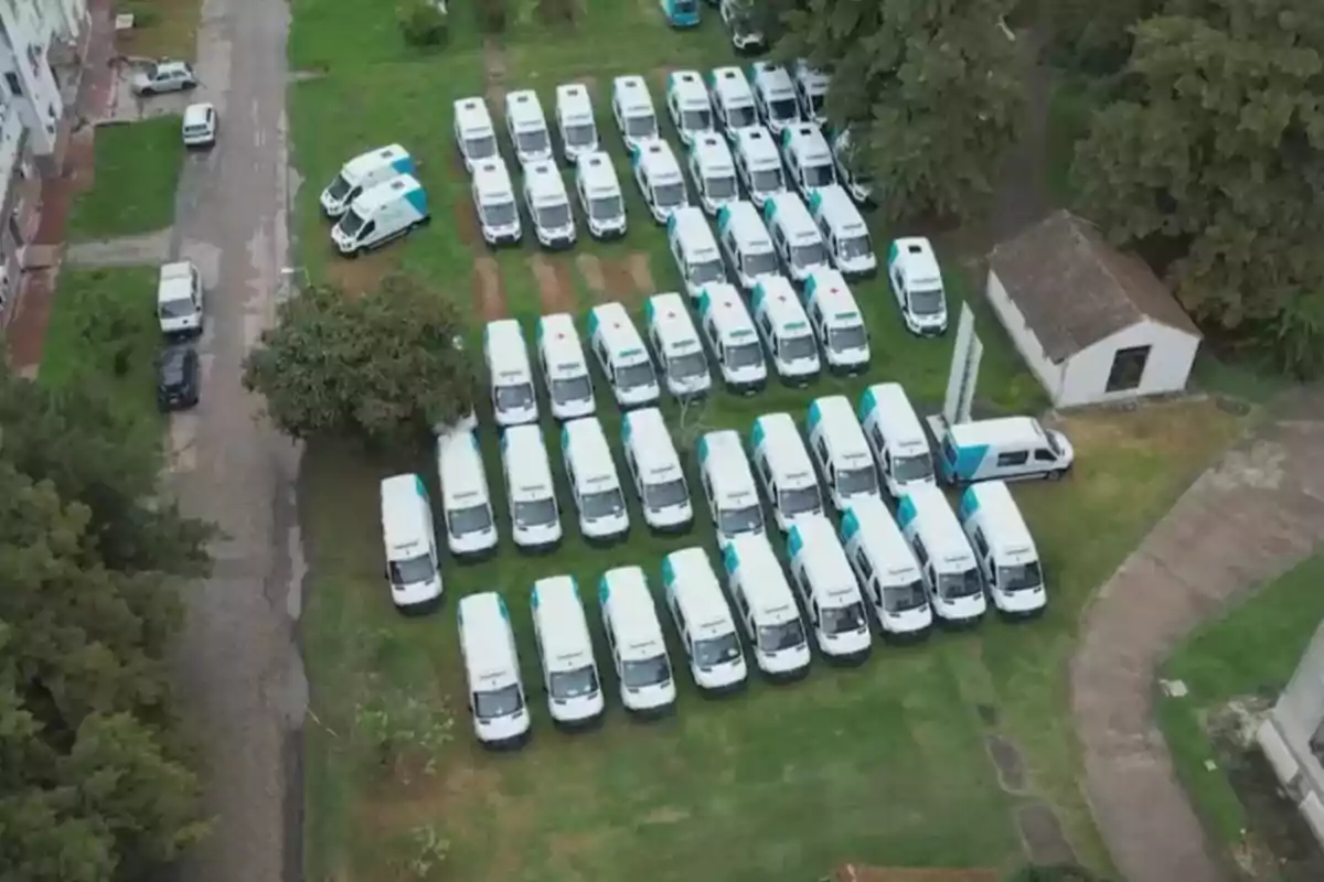 Vista aérea de varias ambulancias blancas estacionadas en un área verde junto a un edificio pequeño.