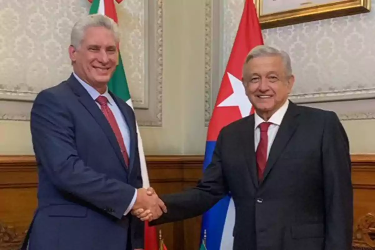 Dos hombres de traje se dan la mano frente a banderas de México y Cuba.