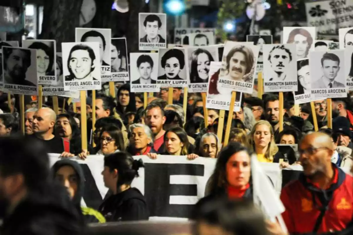A group of people participates in a march holding signs with photographs of missing persons, in what appears to be a demonstration for memory and justice. A group of people participates in a march holding signs with photographs of missing persons, in what appears to be a demonstration for memory and justice.