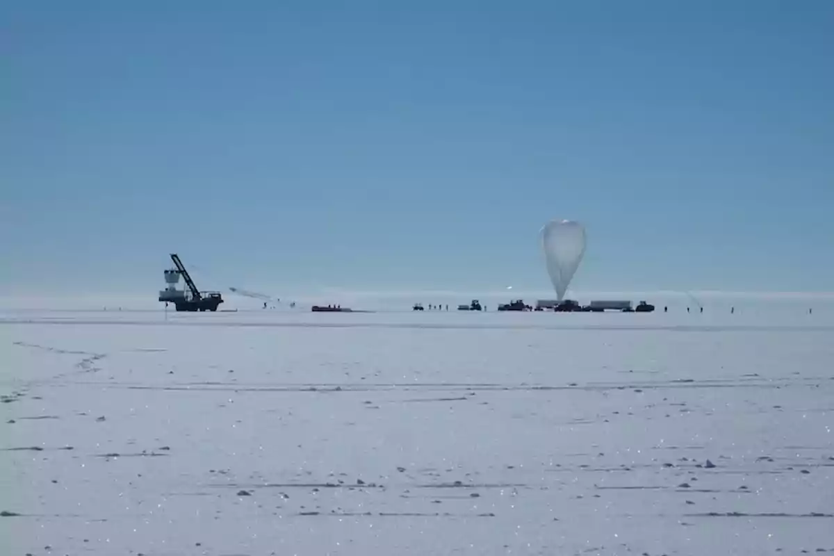 Vehículos y personas en una superficie nevada junto a un gran globo de helio preparándose para el lanzamiento bajo un cielo despejado Vehículos y personas en una superficie nevada junto a un gran globo de helio preparándose para el lanzamiento bajo un cielo despejado