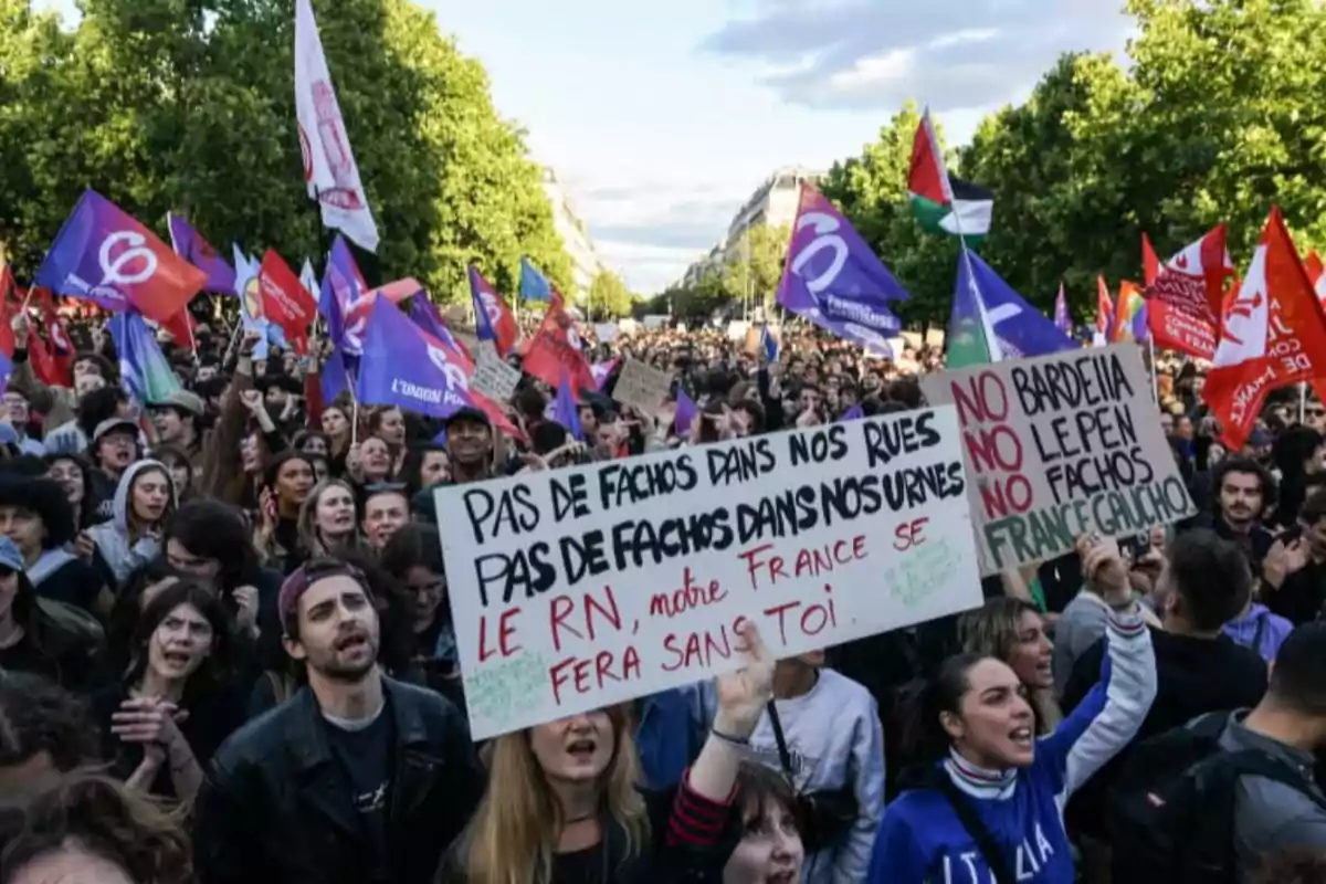 Manifestación multitudinaria en la calle con personas sosteniendo pancartas y banderas de colores, expresando mensajes en contra de la extrema derecha en Francia. Manifestación multitudinaria en la calle con personas sosteniendo pancartas y banderas de colores, expresando mensajes en contra de la extrema derecha en Francia.