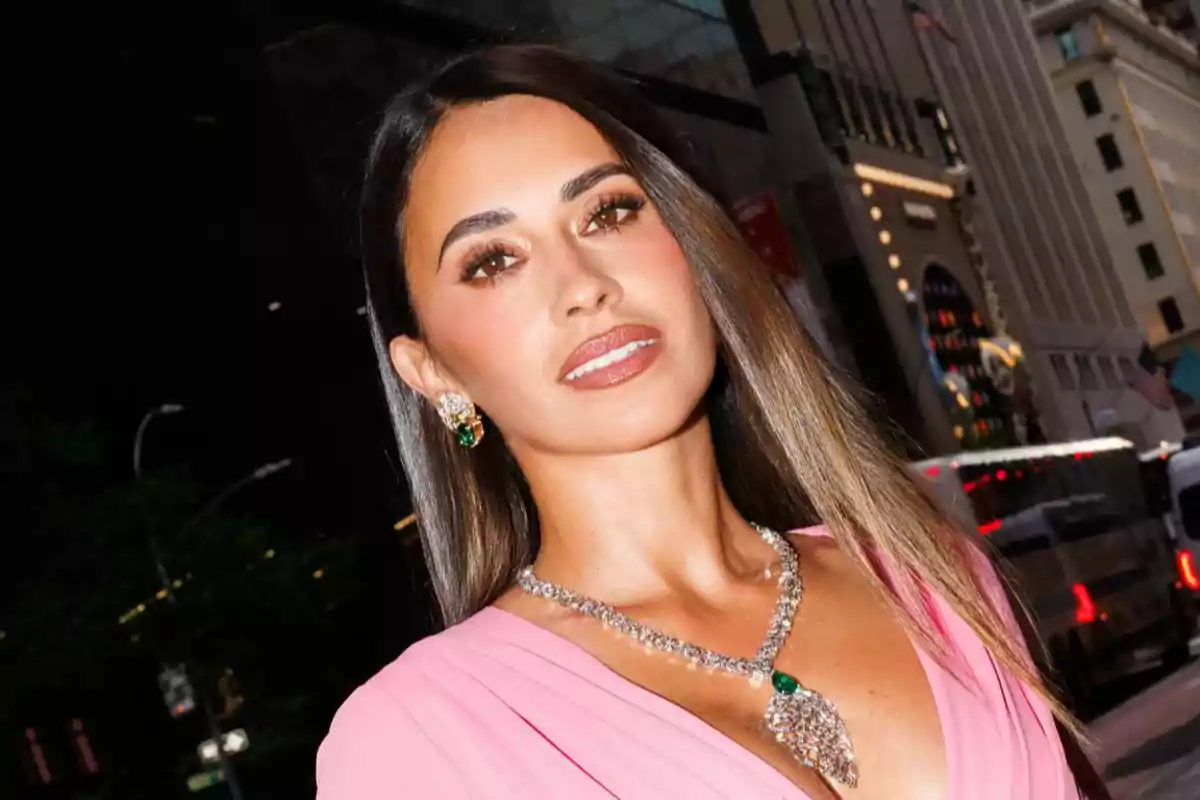 A woman in a pink dress and jewelry poses on a city street at night.