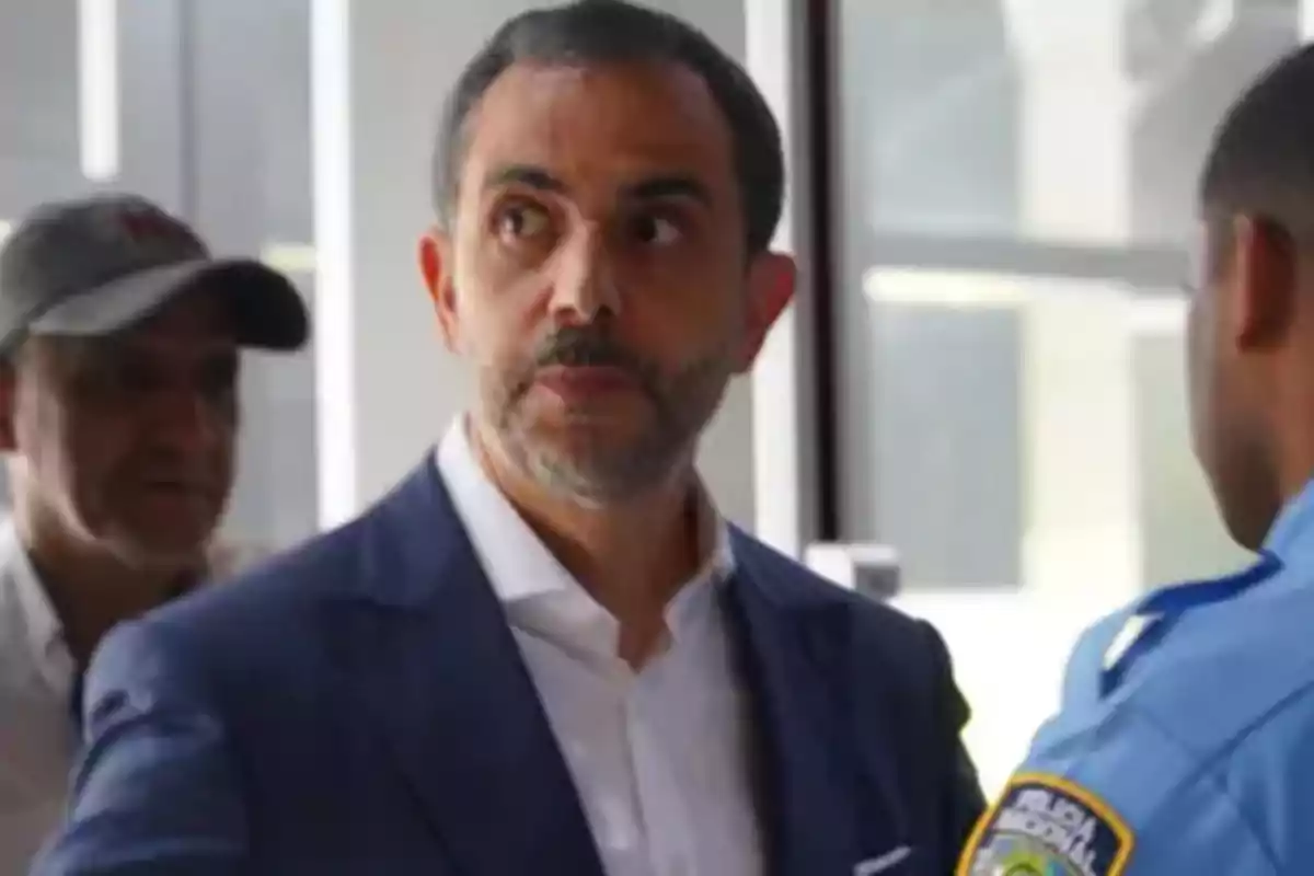 Hombre de barba con saco azul y camisa blanca hablando con un oficial de policía