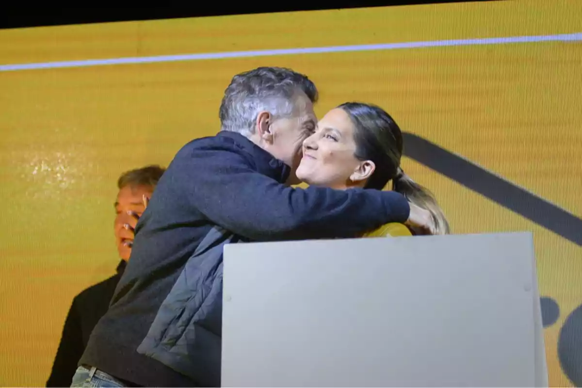Una persona abrazando a otra en un escenario con fondo amarillo. Una persona abrazando a otra en un escenario con fondo amarillo.
