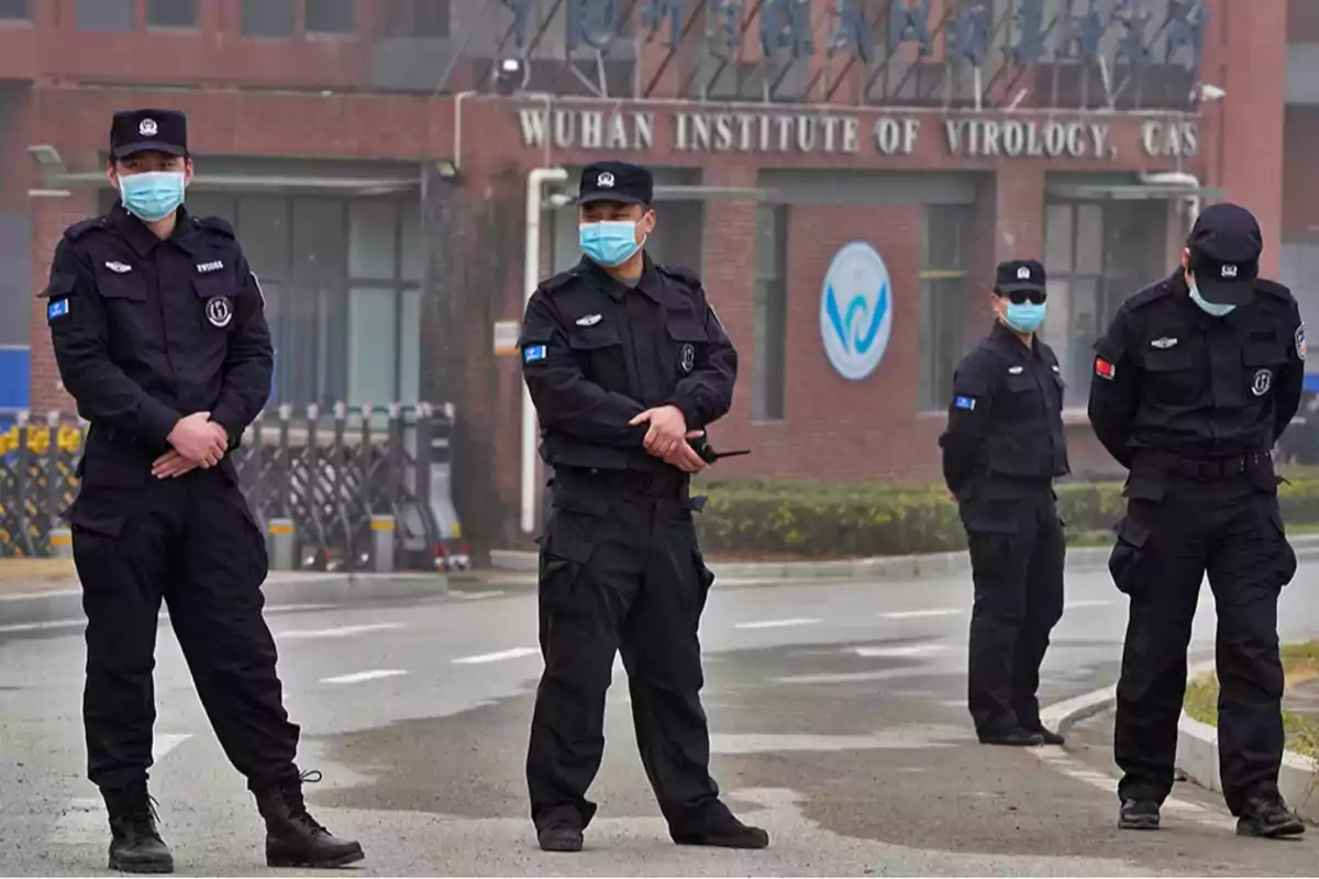 Un grupo de guardias de seguridad con mascarillas está de pie frente a un edificio con el letrero "Wuhan Institute of Virology".