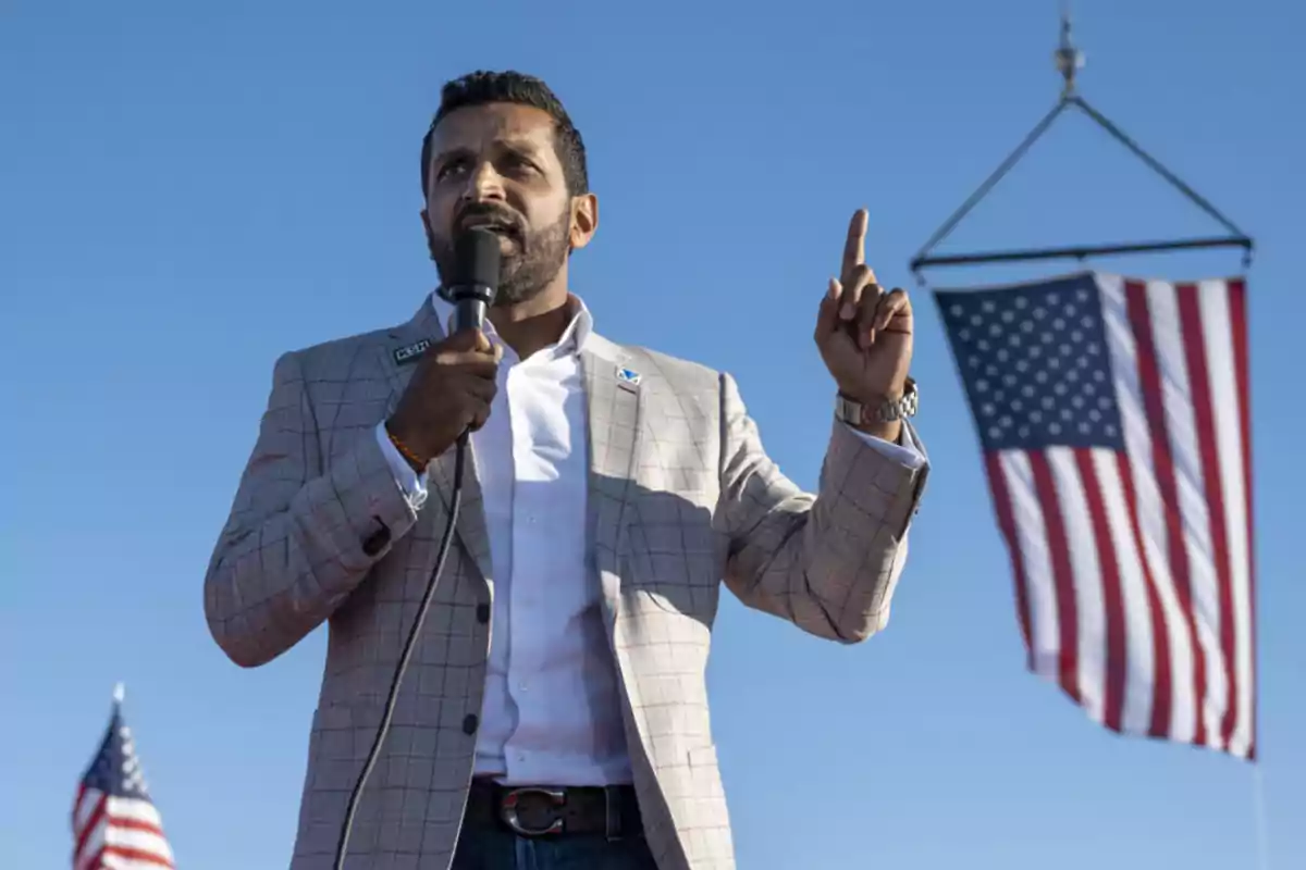 Hombre hablando en un micrófono con una bandera de Estados Unidos de fondo.