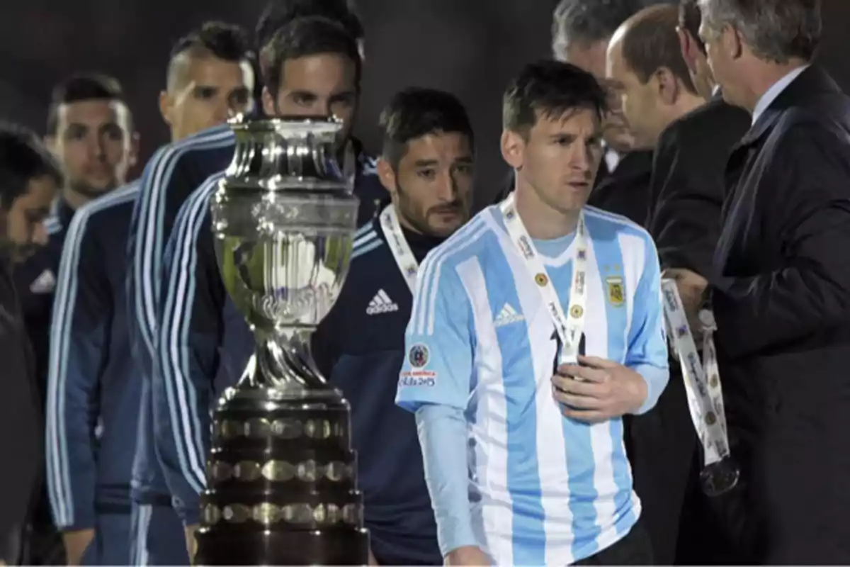 Players of the Argentine national soccer team walk past a trophy with serious expressions and medals around their necks. Players of the Argentine national soccer team walk past a trophy with serious expressions and medals around their necks.