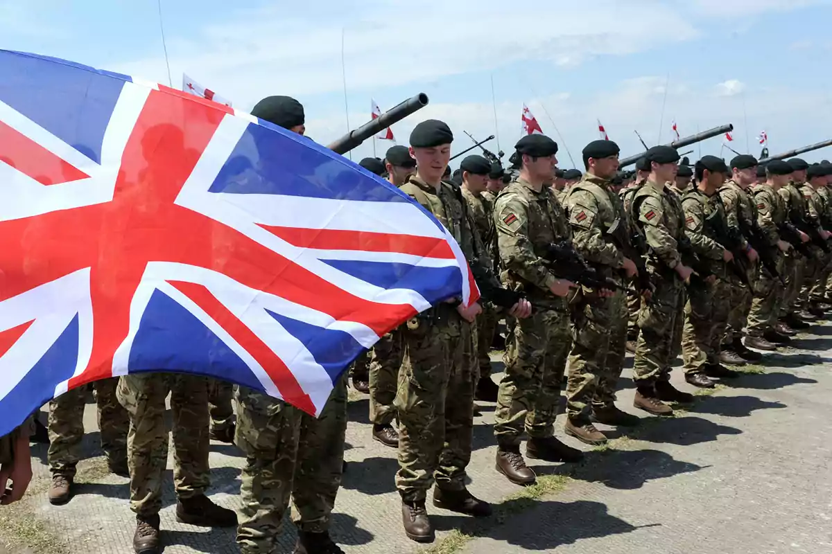 Soldados en formación con uniformes militares y una bandera del Reino Unido ondeando al frente.