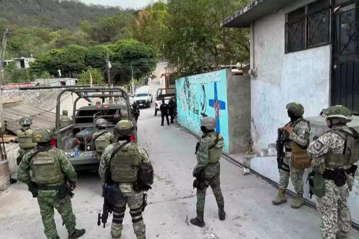 A group of soldiers with tactical gear is on a street, next to military vehicles, in an urban environment with graffiti on the walls. A group of soldiers with tactical gear is on a street, next to military vehicles, in an urban environment with graffiti on the walls.