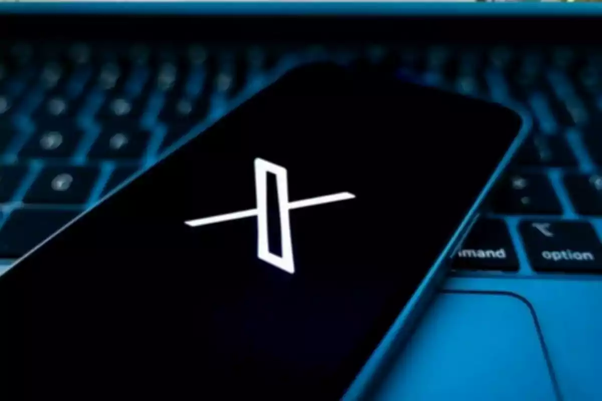 Mobile phone with the X logo on the screen over a computer keyboard lit in blue Mobile phone with the X logo on the screen over a computer keyboard lit in blue