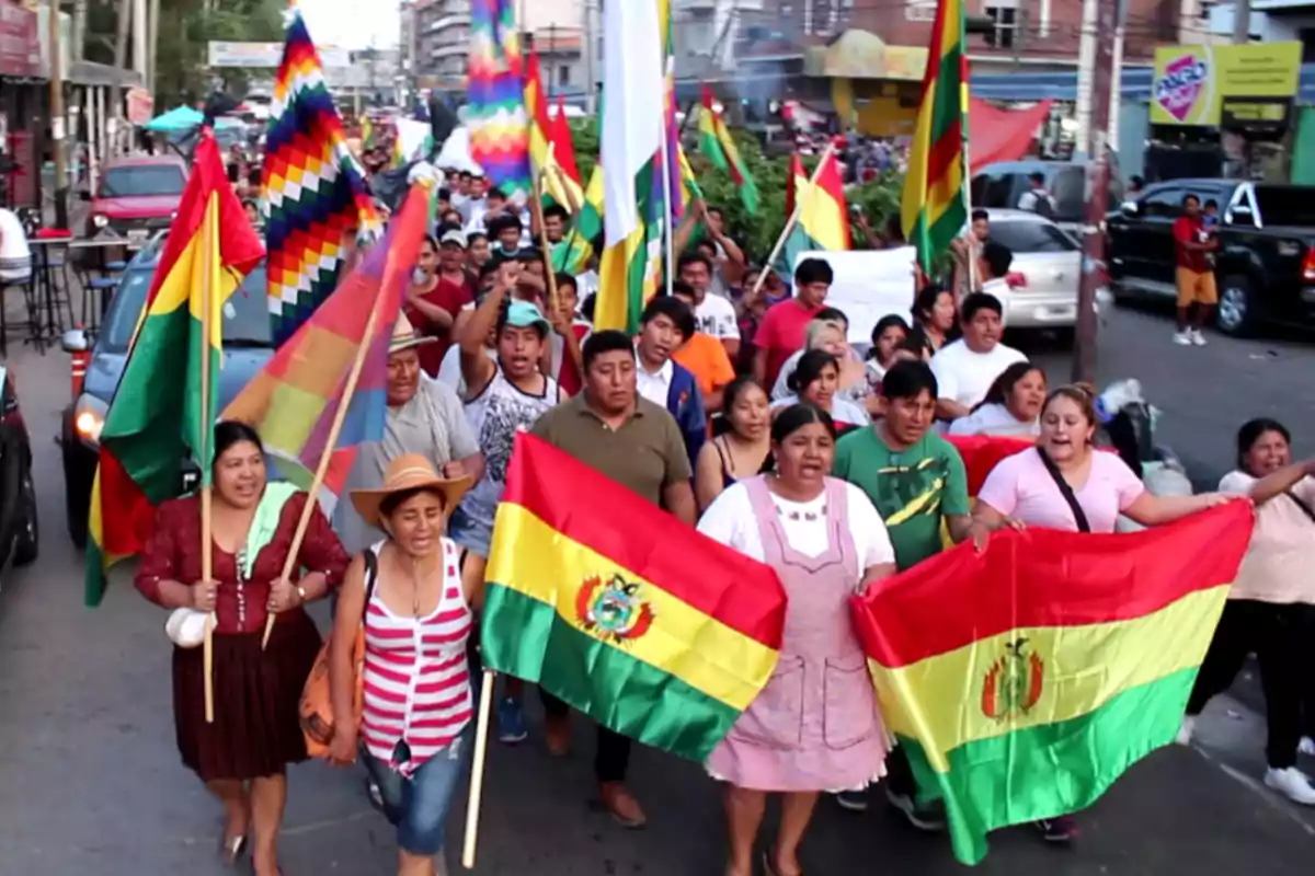 Un grupo de personas marcha por una calle llevando banderas de Bolivia y la bandera Wiphala.