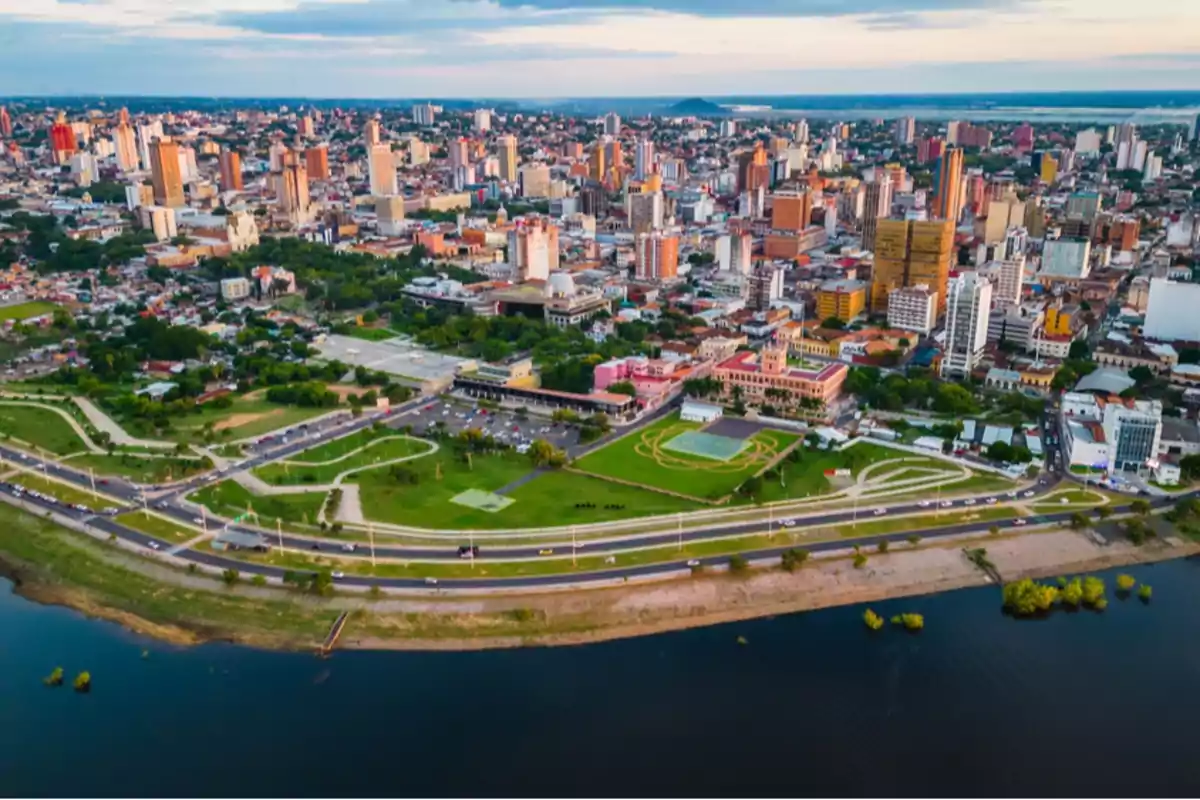 Vista aérea de una ciudad con edificios altos, áreas verdes y un río en primer plano.