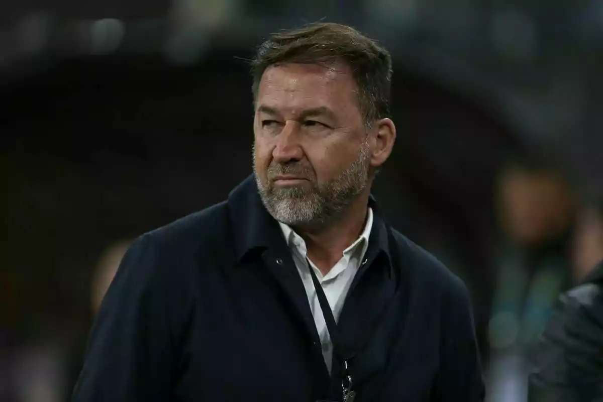 Middle-aged man with a beard and short hair looking to the side with a serious expression in a dark setting