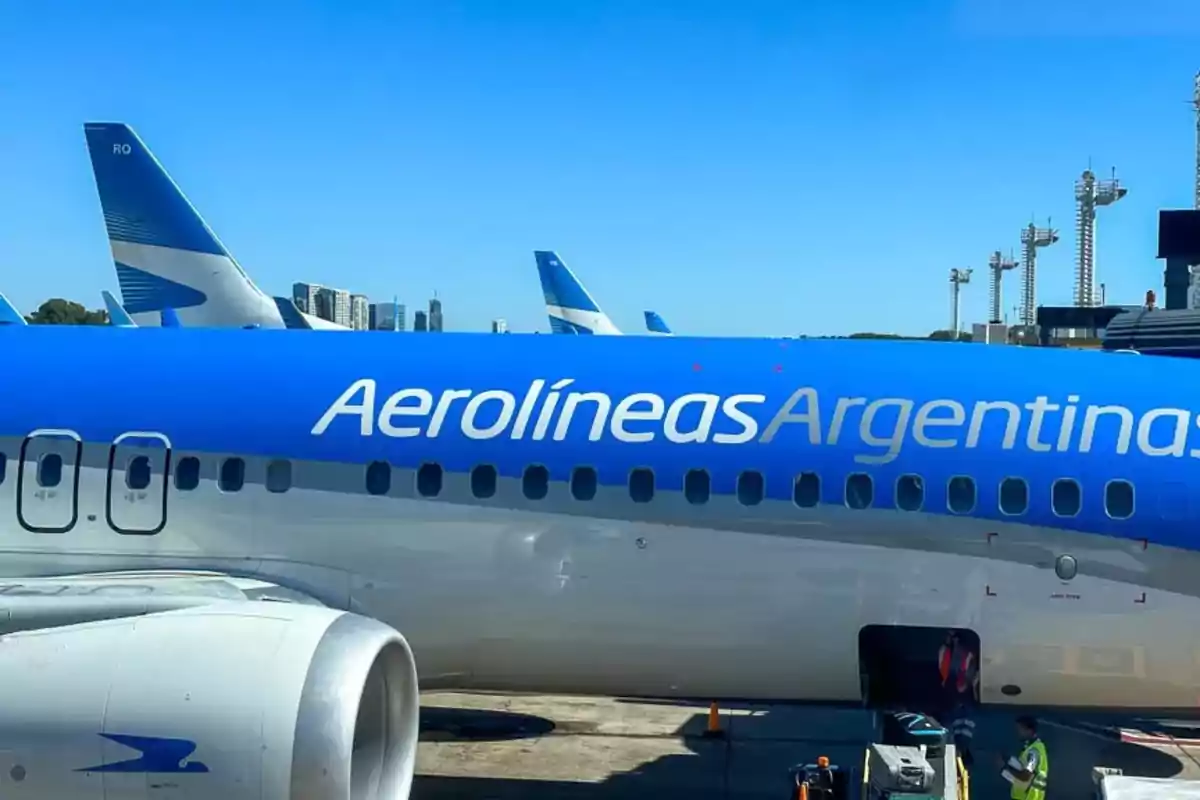 Un avión de Aerolíneas Argentinas en el aeropuerto con el cielo despejado y edificios al fondo.