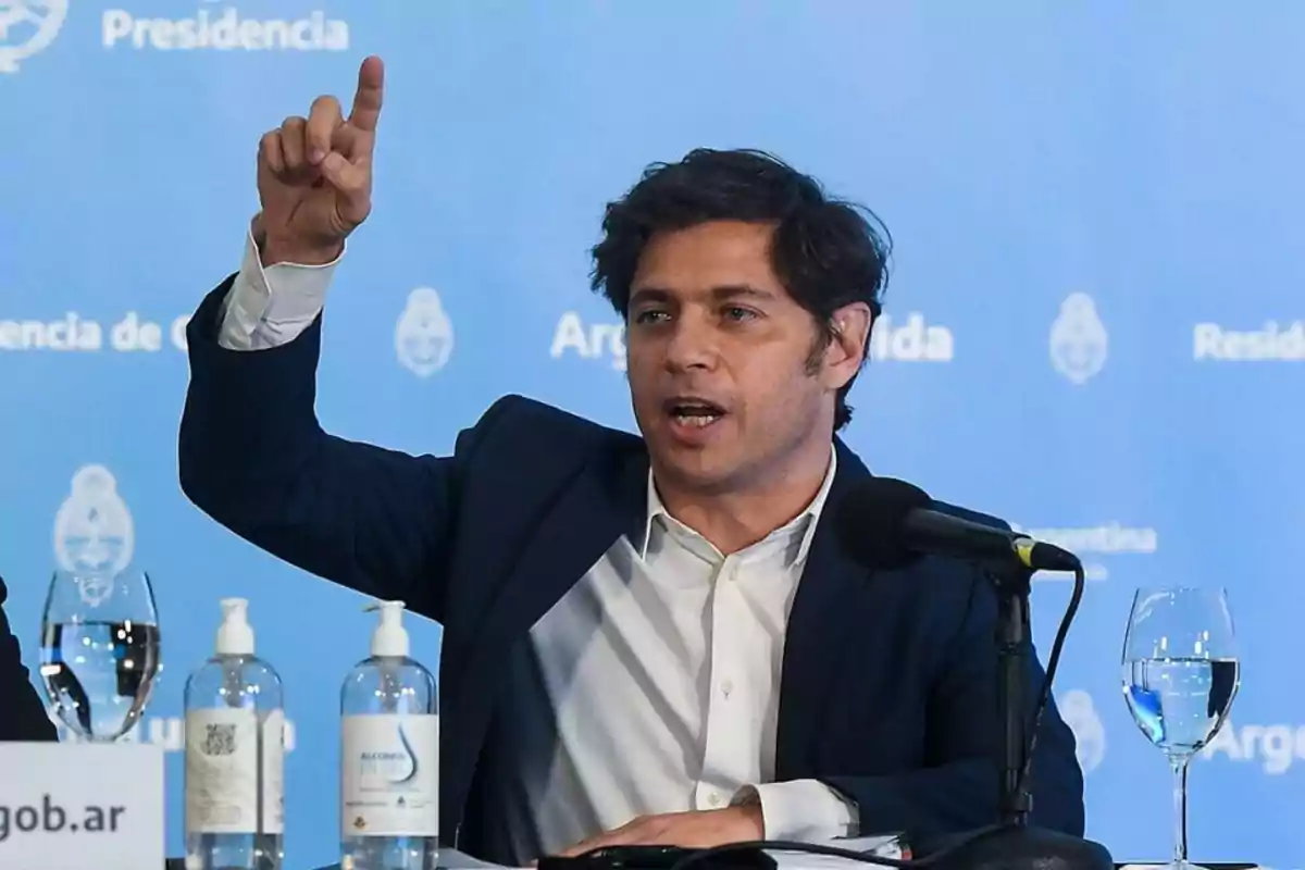 Un hombre hablando en una conferencia de prensa con un fondo azul que dice "Presidencia" y "Argentina", con botellas de alcohol en gel y un micrófono frente a él.