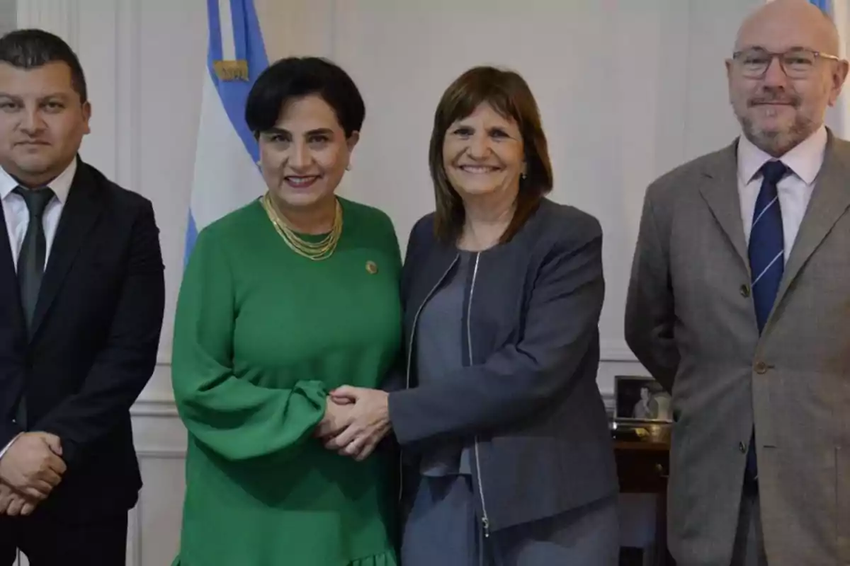 Four people pose together in a formal setting with a flag in the background.