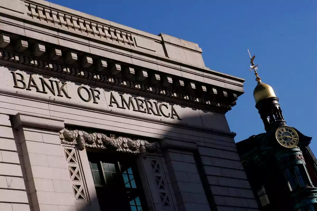 Fachada de un edificio del Bank of America con un reloj y una veleta en la parte superior de una torre adyacente bajo un cielo despejado.