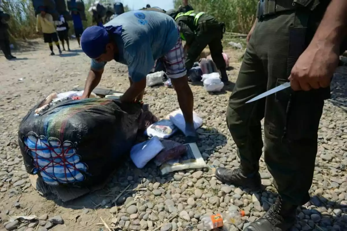 Un grupo de personas revisa un paquete grande en un camino de piedras, mientras un hombre sostiene un cuchillo.