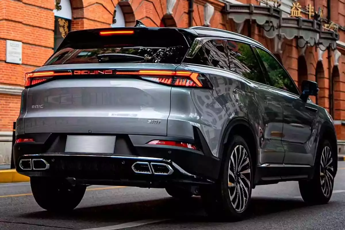 Modern-design silver SUV driving down a street with brick buildings in the background Modern-design silver SUV driving down a street with brick buildings in the background