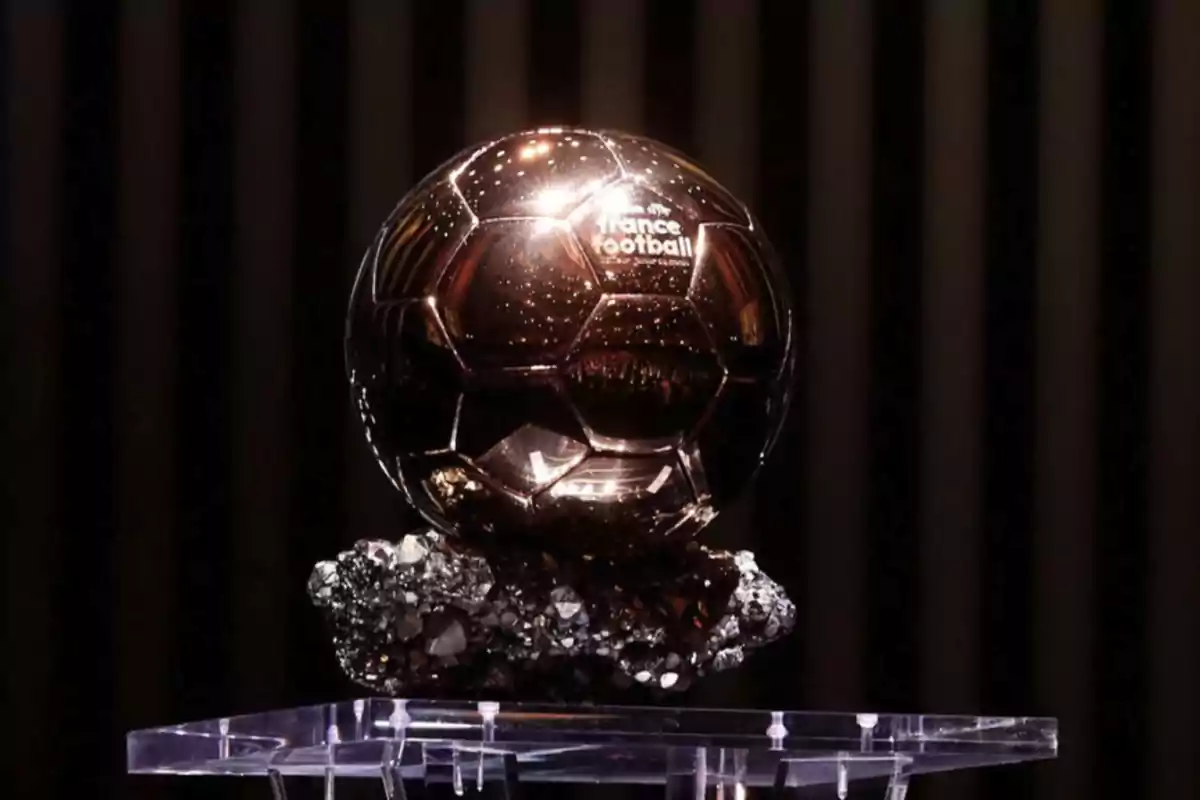 Trofeo dorado con forma de balón de fútbol sobre una base de cristal y mineral oscuro.