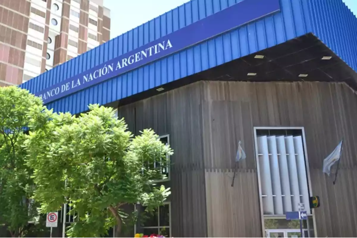 Fachada de una sucursal del Banco de la Nación Argentina con árboles y banderas argentinas en la entrada