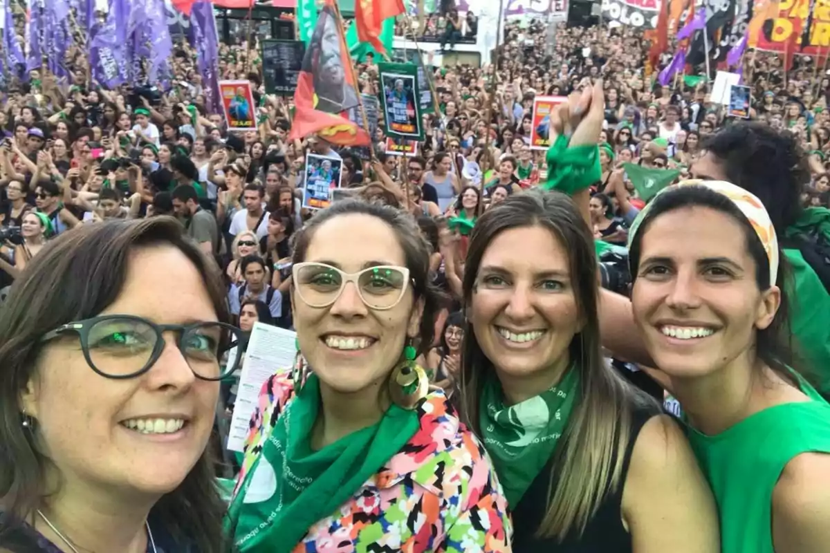 Un grupo de personas sonríe a la cámara en una manifestación con una multitud al fondo, algunas llevan pañuelos verdes y hay banderas y carteles en el aire. Un grupo de personas sonríe a la cámara en una manifestación con una multitud al fondo, algunas llevan pañuelos verdes y hay banderas y carteles en el aire.