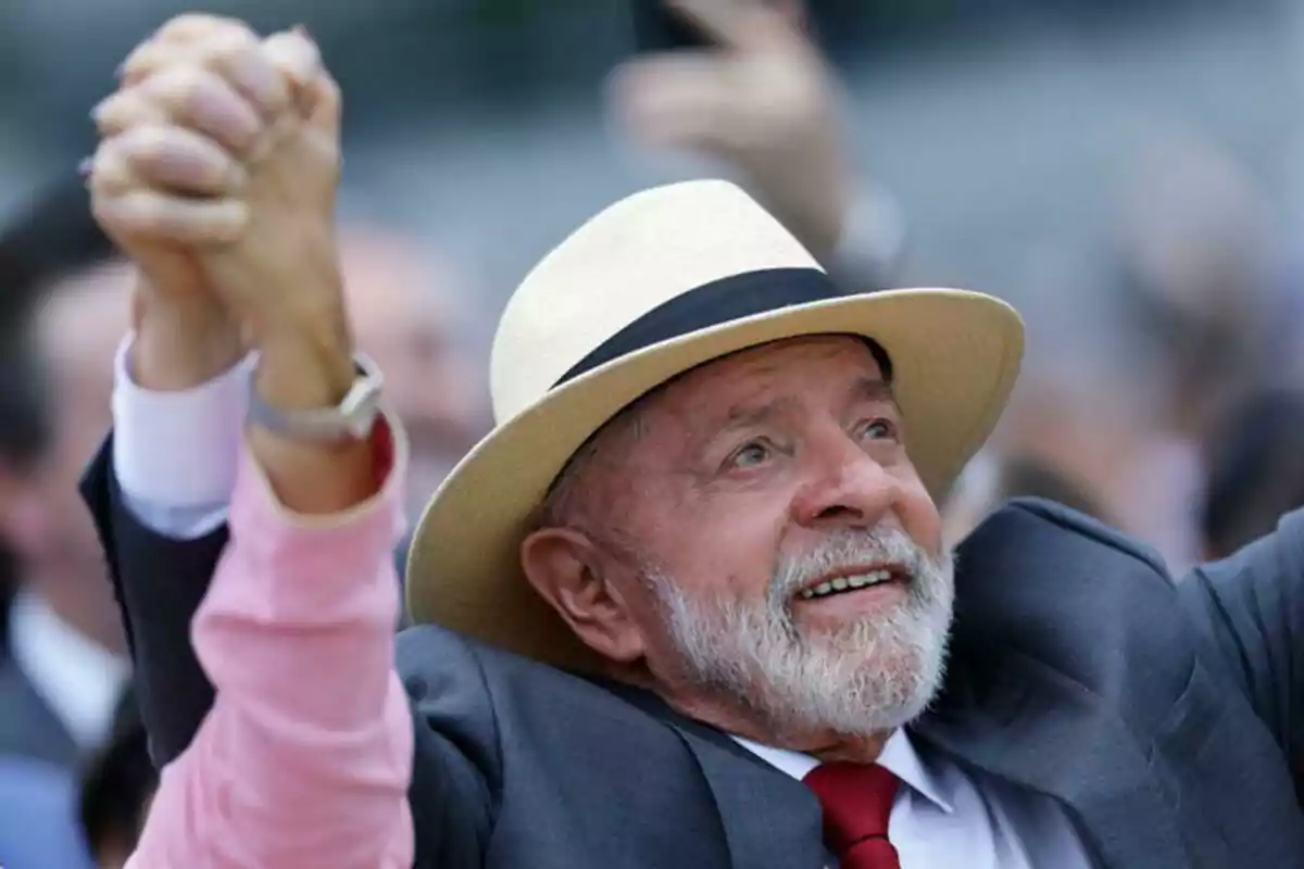 Un hombre sonriente con barba y sombrero sostiene la mano de otra persona en un gesto de celebración.