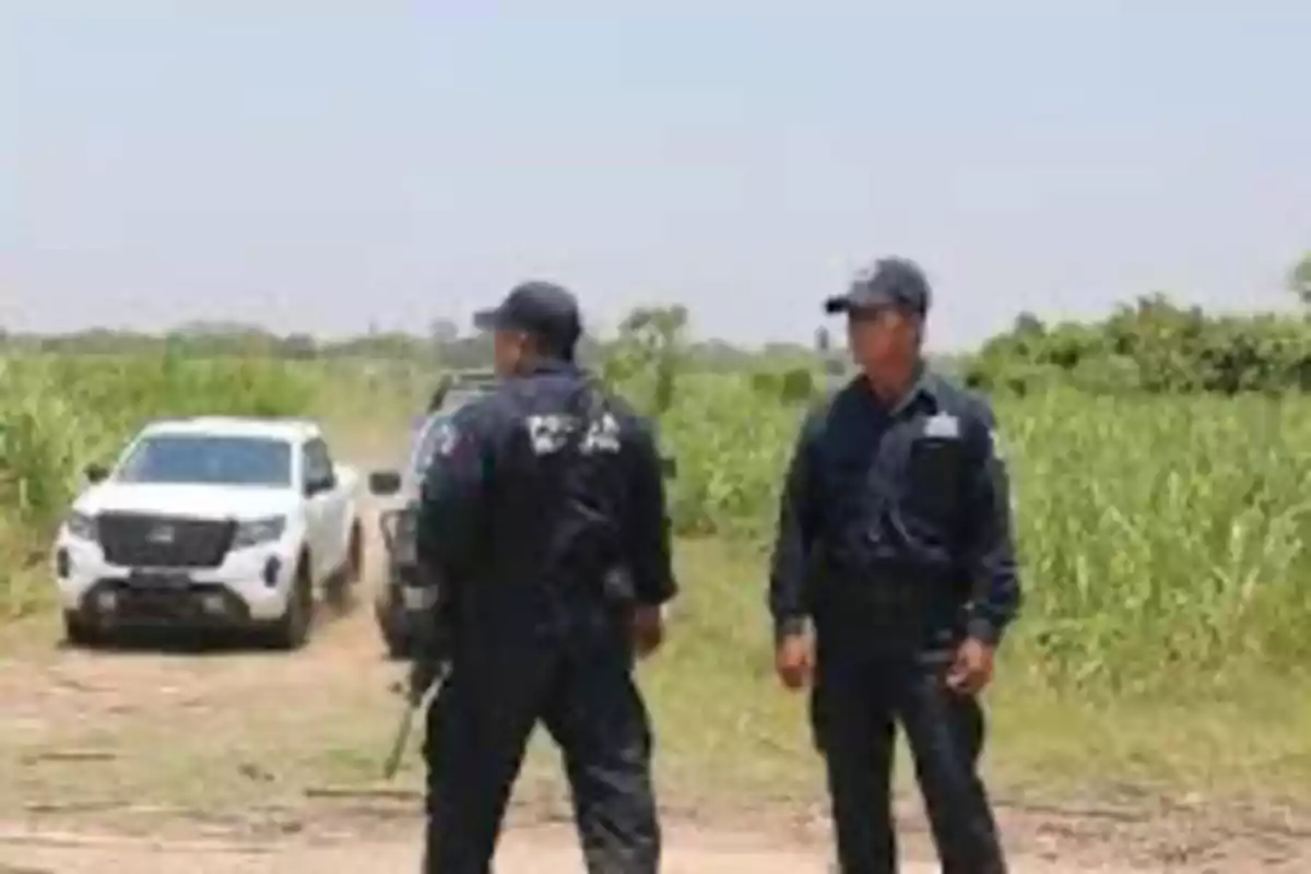 Two police officers standing on a dirt road with a white vehicle in the background and vegetation around. Two police officers standing on a dirt road with a white vehicle in the background and vegetation around.