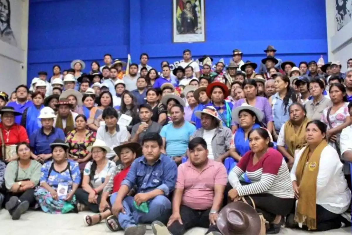 Un grupo numeroso de personas posando juntas en un salón con paredes azules y un retrato en la pared.