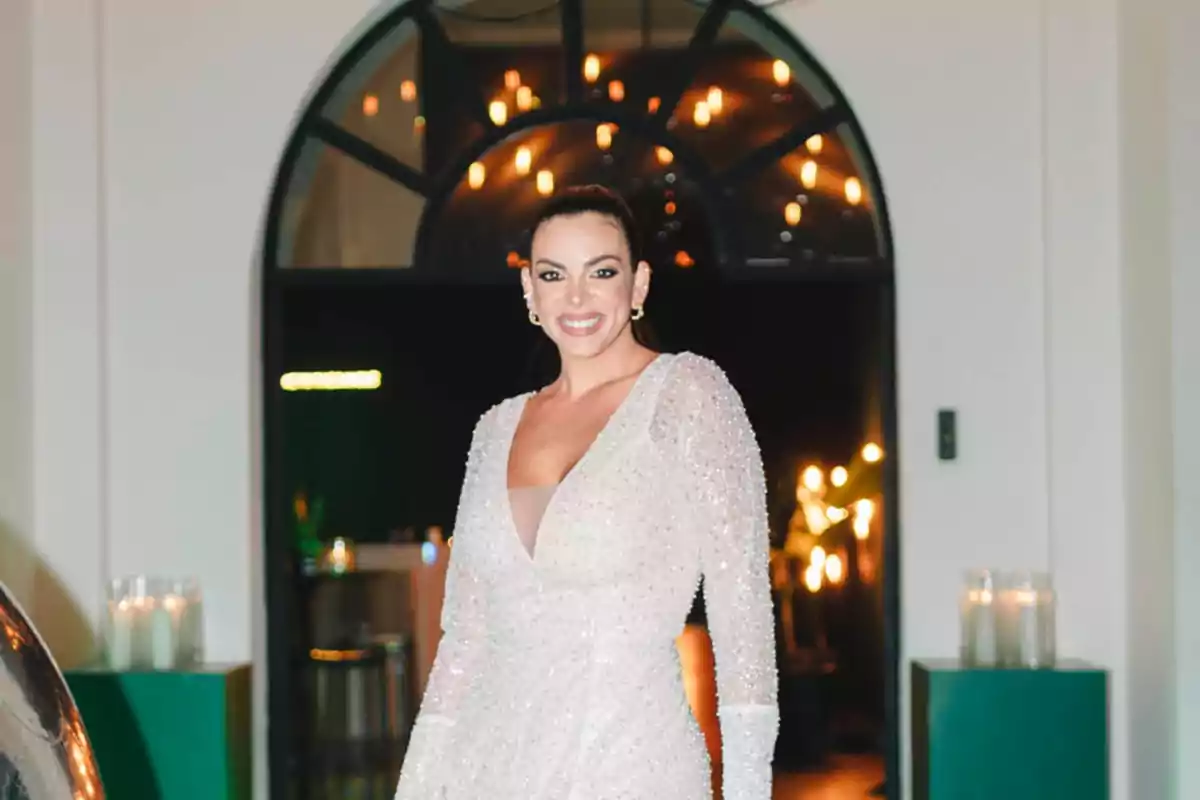 Una persona con un vestido brillante posando frente a una puerta arqueada iluminada.