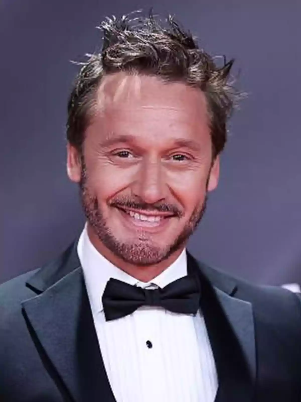 Un hombre con esmoquin y pajarita sonriendo en un evento formal. Un hombre con esmoquin y pajarita sonriendo en un evento formal.