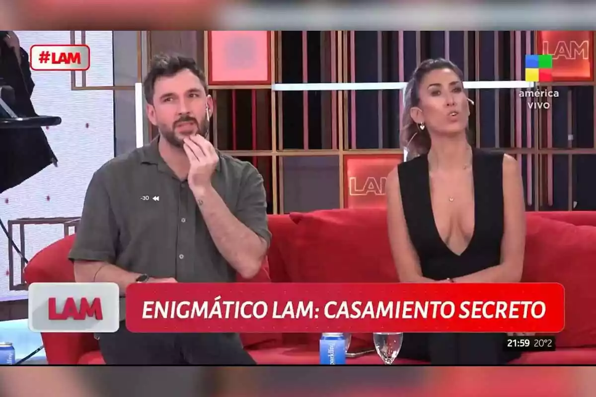 Dos personas sentadas en un set de televisión con un letrero que dice Dos personas sentadas en un set de televisión con un letrero que dice