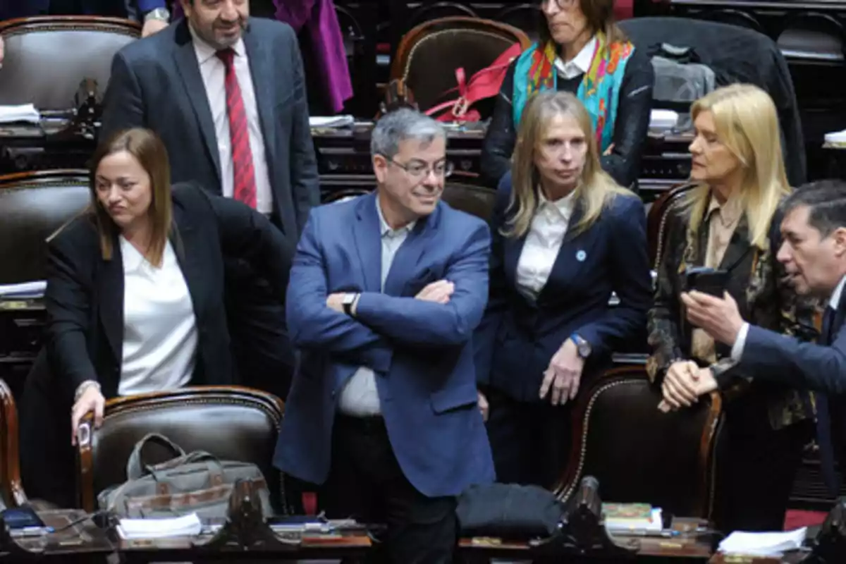 Un grupo de personas de pie y conversando en un entorno formal con sillas y mesas.