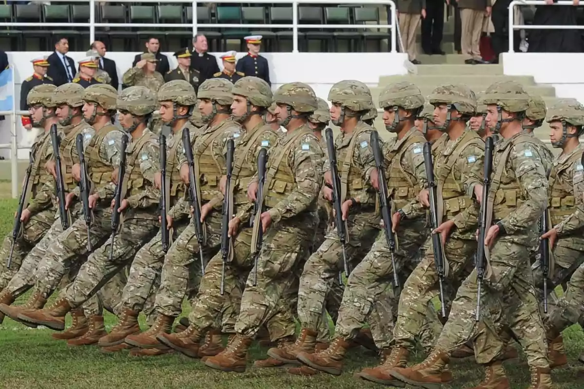 A group of soldiers marches in formation during a military parade, wearing camouflage uniforms and helmets, while carrying rifles in their hands.