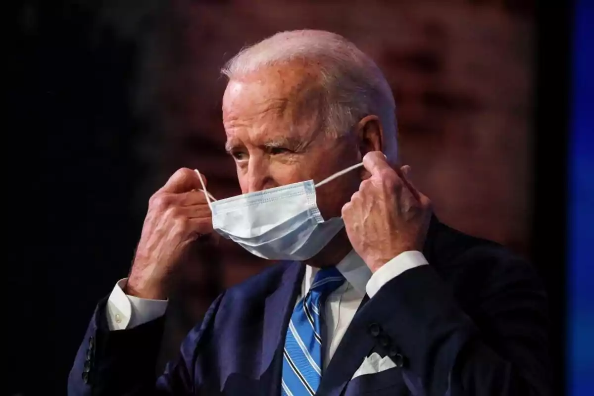 An older man in a blue suit and a striped tie is putting on a mask. An older man in a blue suit and a striped tie is putting on a mask.