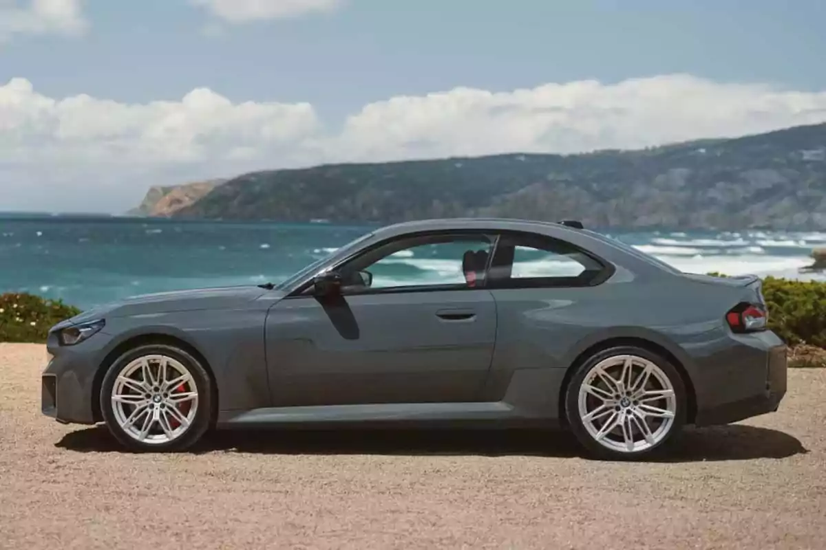Gray sports car parked by the sea with mountains in the background Gray sports car parked by the sea with mountains in the background