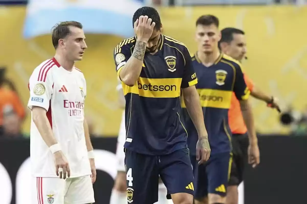 A Boca Juniors player covers his face with his hand while a Benfica footballer watches him during a soccer match. A Boca Juniors player covers his face with his hand while a Benfica footballer watches him during a soccer match.