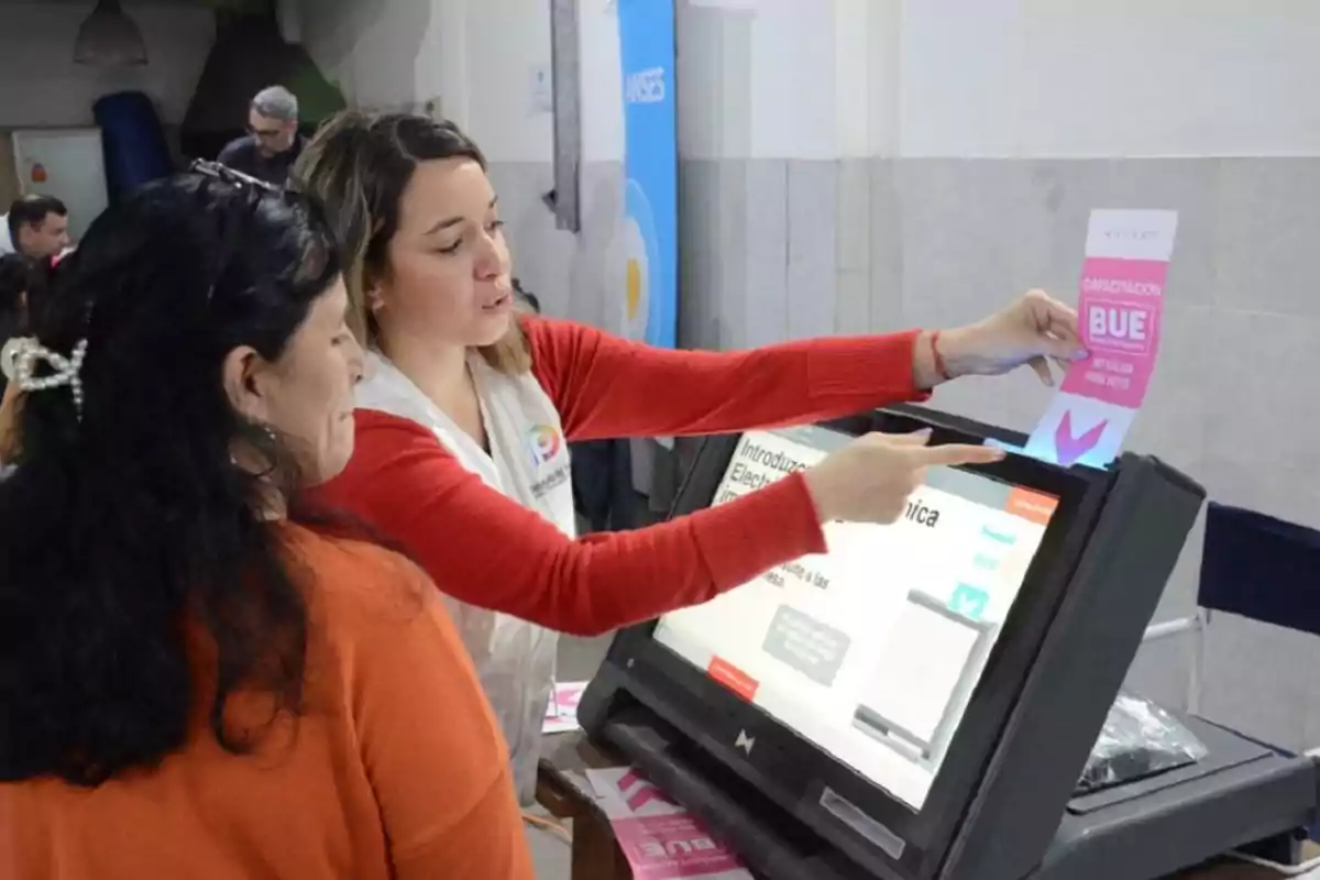 Una mujer está mostrando a otra cómo usar una máquina de votación electrónica en un entorno de capacitación. Una mujer está mostrando a otra cómo usar una máquina de votación electrónica en un entorno de capacitación.