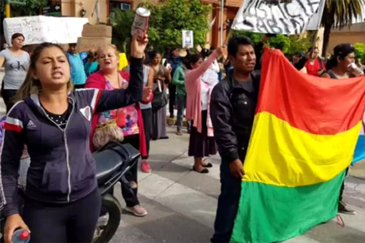 Un grupo de personas participa en una manifestación, algunas sostienen carteles y una bandera con los colores rojo, amarillo y verde.