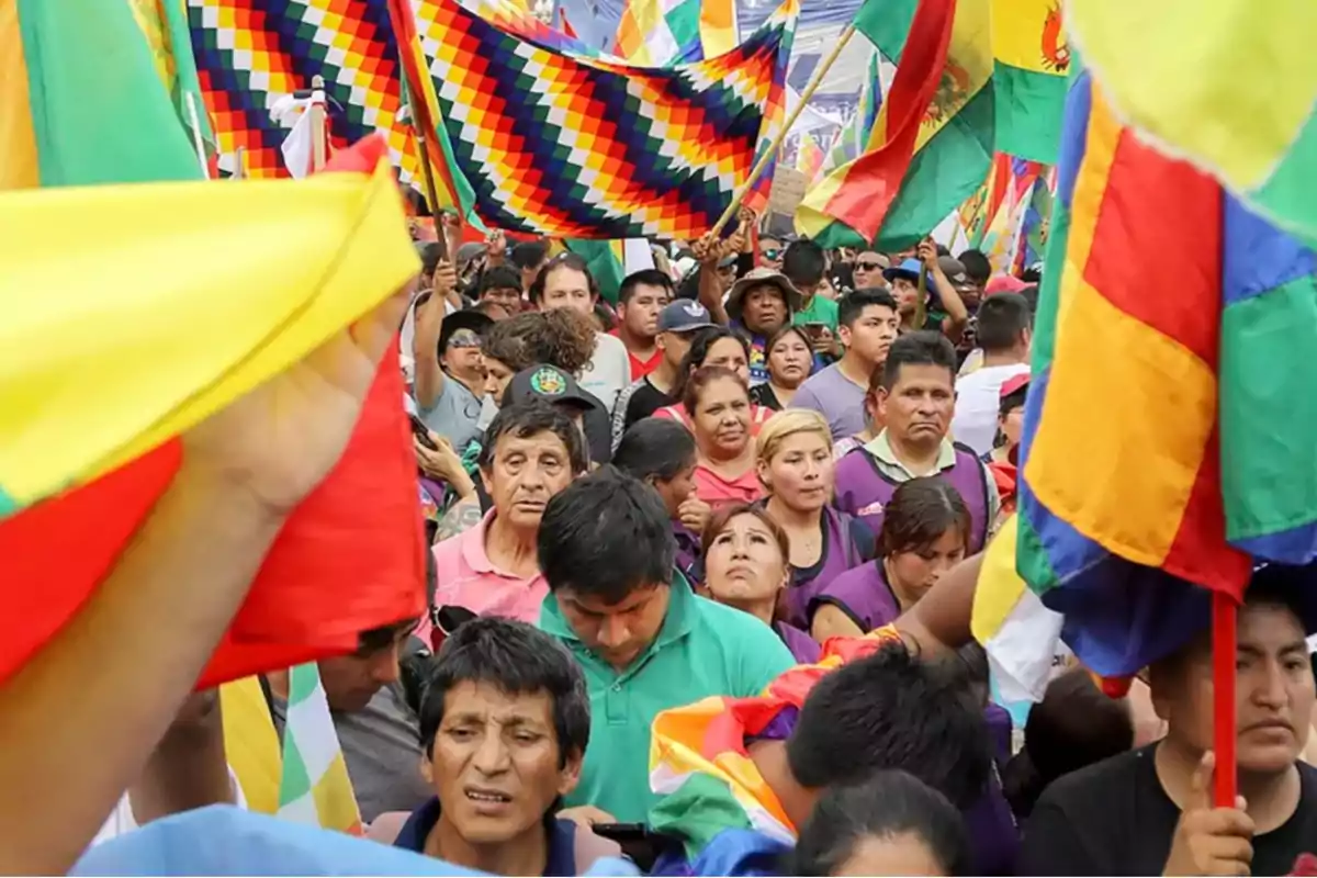 Una multitud de personas participando en una manifestación con banderas coloridas.