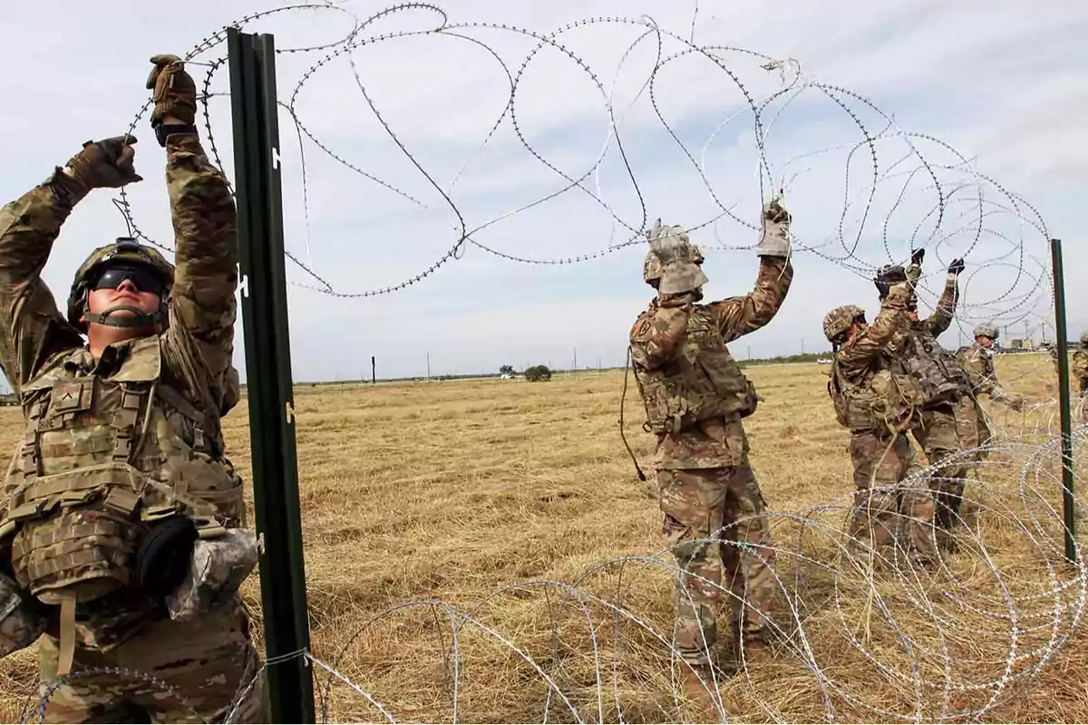 Soldados instalando una cerca de alambre de púas en un campo abierto.