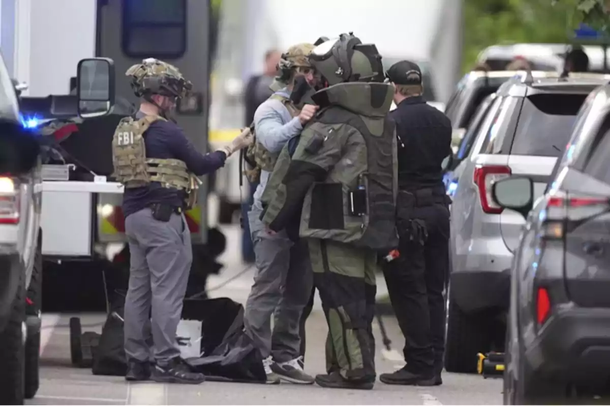 Agentes del FBI y personal especializado preparan a un miembro del equipo antibombas que viste un traje protector en una calle rodeada de vehículos policiales