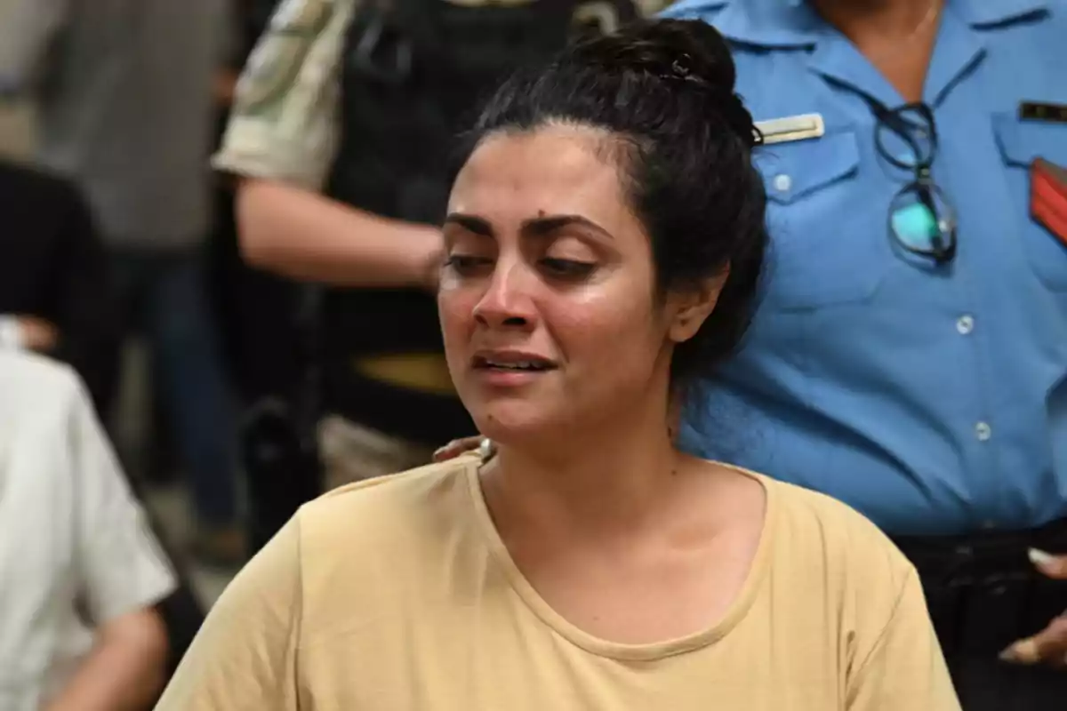 Mujer con expresión de tristeza y ojos llorosos acompañada por una persona con uniforme azul