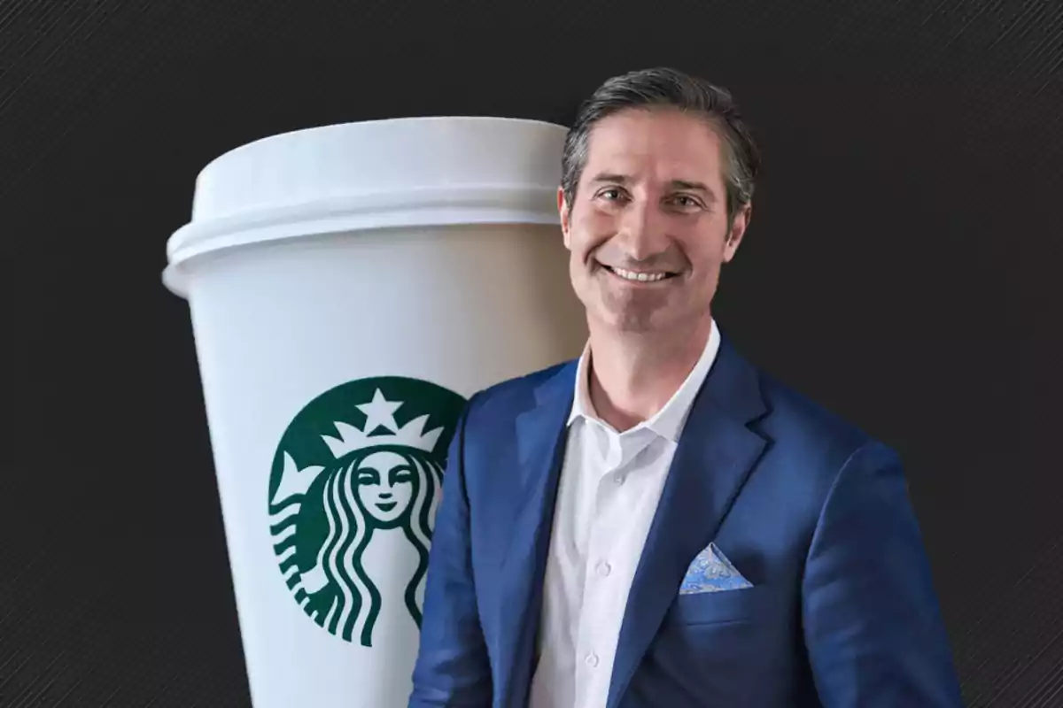 Hombre de traje azul sonriendo frente a un vaso de Starbucks.