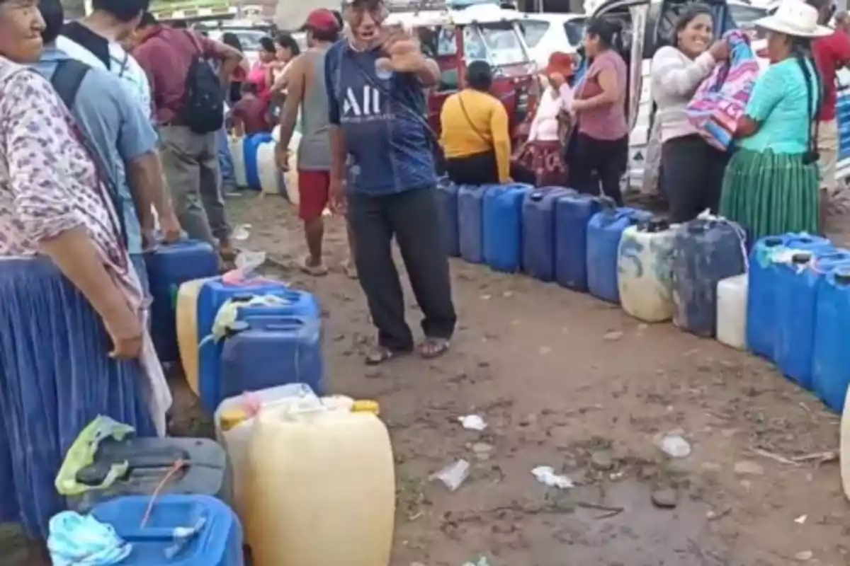 Personas haciendo fila con bidones de plástico en un área al aire libre. Personas haciendo fila con bidones de plástico en un área al aire libre.