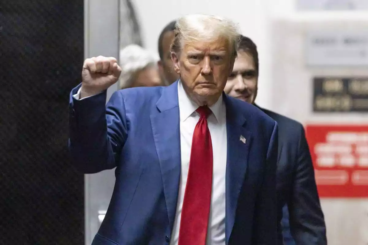 Hombre de traje azul y corbata roja levantando el puño mientras camina por un pasillo.