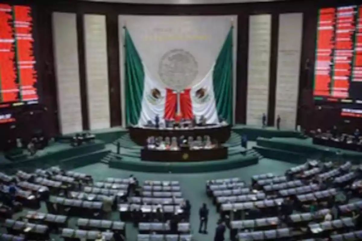 Una sala de sesiones con un gran escudo nacional y banderas en el fondo, rodeada de asientos y pantallas electrónicas.