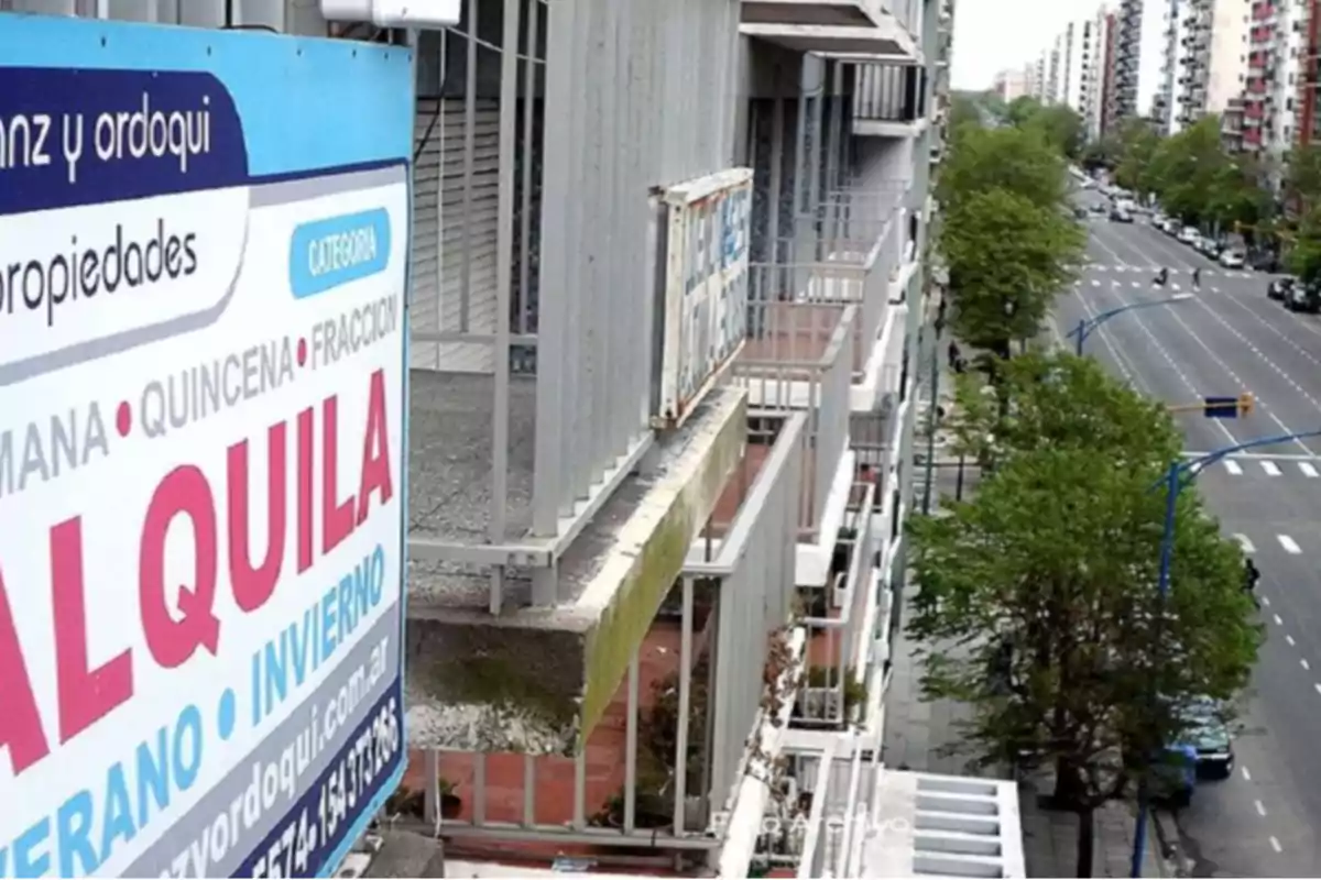 Un cartel de alquiler en un edificio con vista a una avenida arbolada.