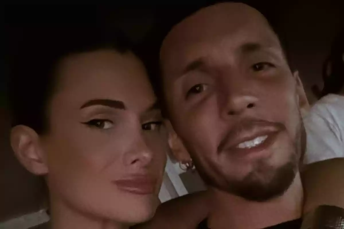 Una pareja sonríe mientras posa para una selfie en un ambiente oscuro.