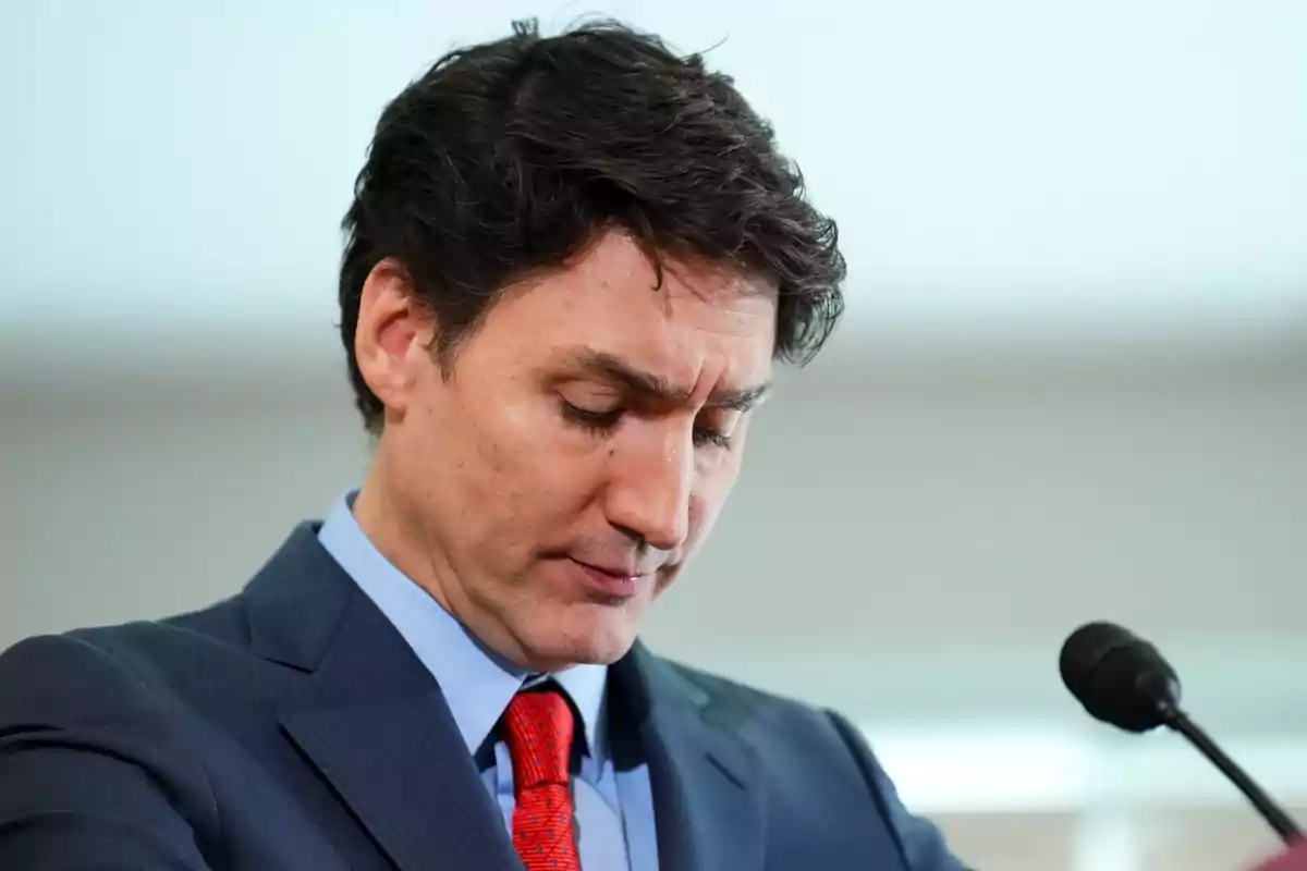 A man in a dark suit and red tie is standing in front of a microphone with his head tilted.